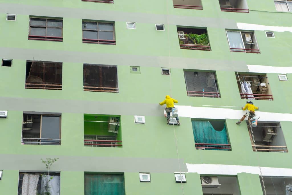Commercial painting workers painting an apartment building green.