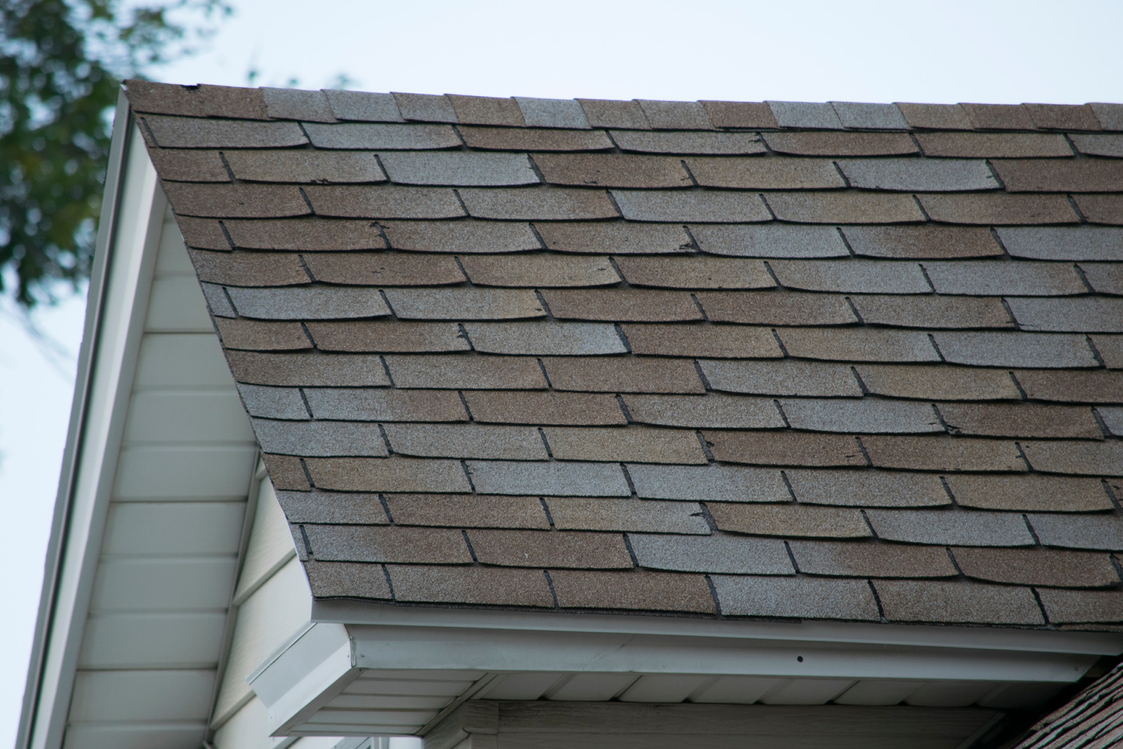 Roof of a residential house showing damage, multiple layers of shingles, missing shingles.